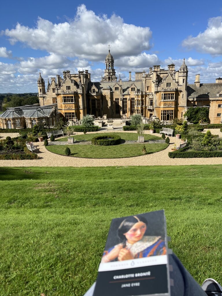 Reading 'Jane Eyre' by Charlotte Brontë while sitting on a bench facing the back of Harlaxton Manor.