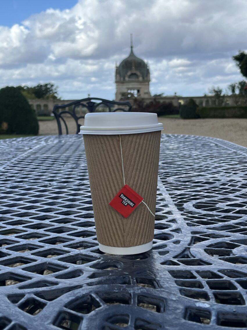 A photo of a paper cup of Yorkshire tea sitting on an outdoor table at Harlaxton Manor.